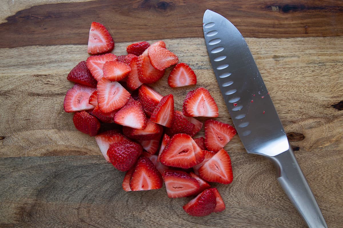 sliced strawberries on a wooden cutting board.