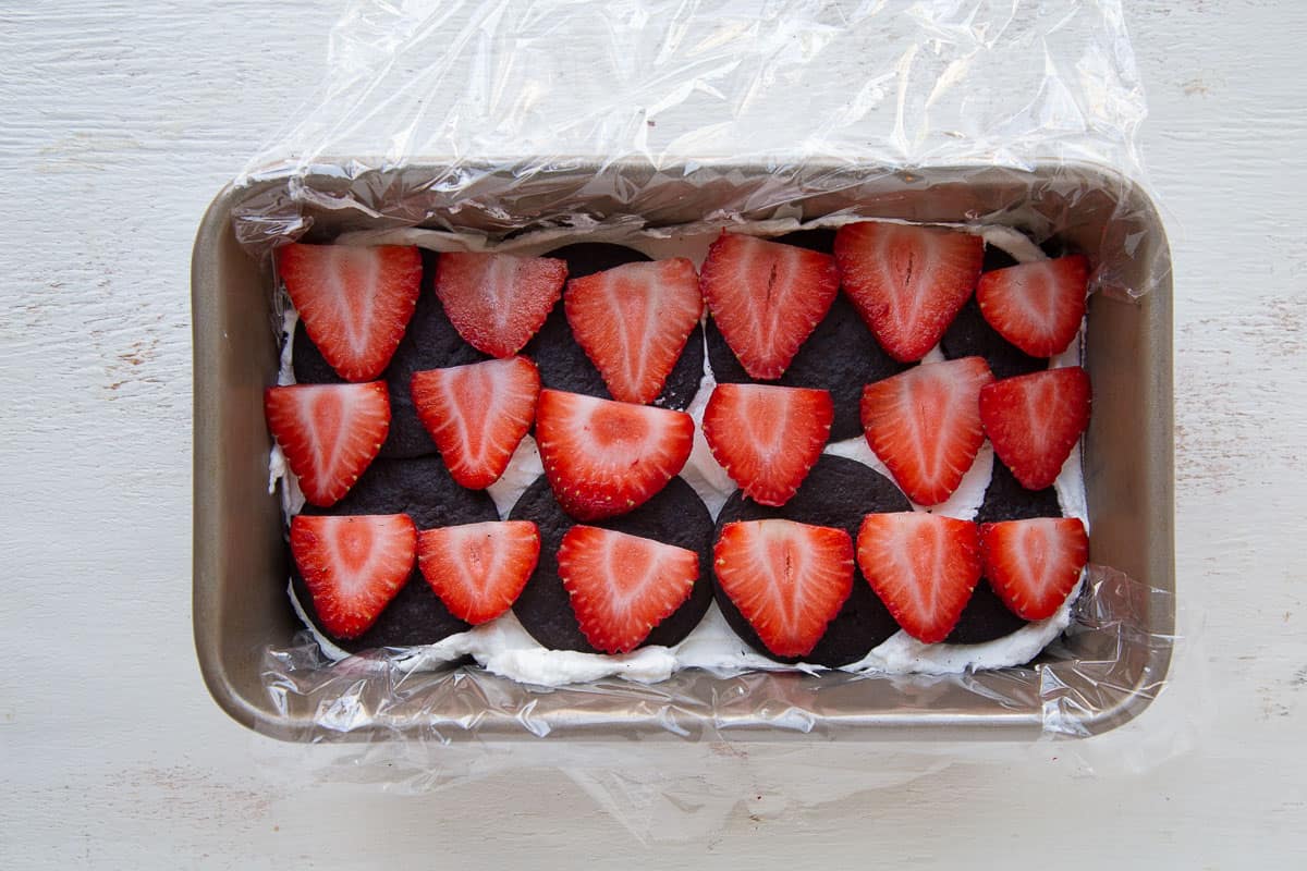 strawberries on top of wafer cookies and whipped cream in a loaf pan.