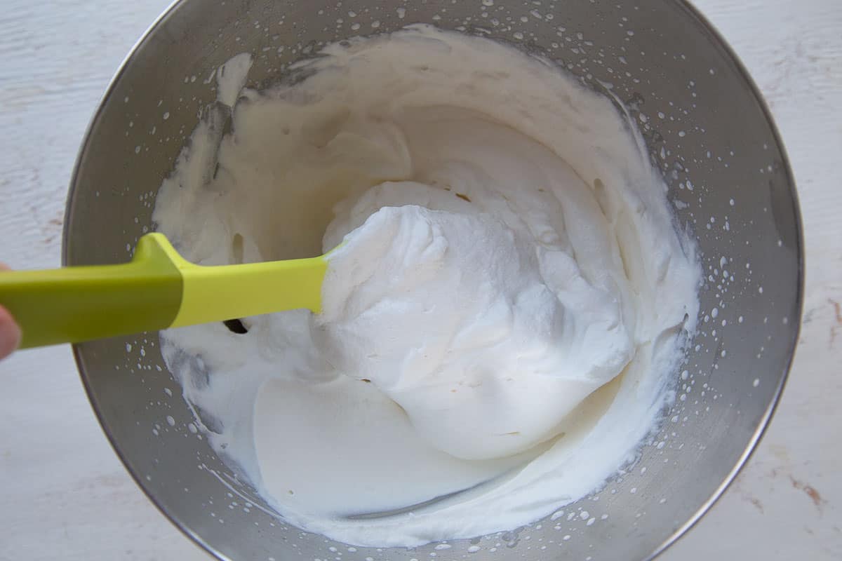 whipped cream in a metal bowl with a yellow spatula.