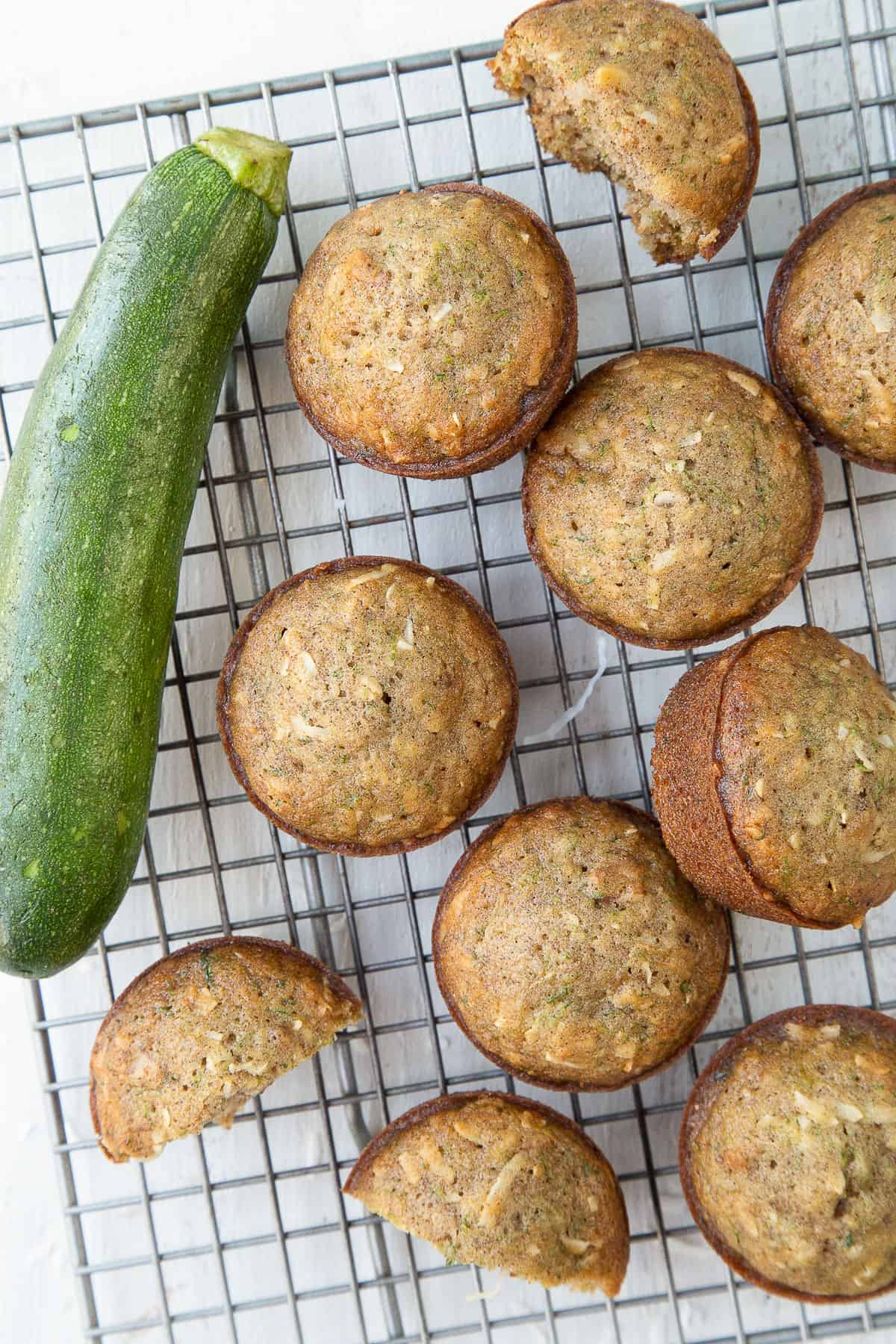 zucchini muffins next to a fresh zucchini on a wire rack.