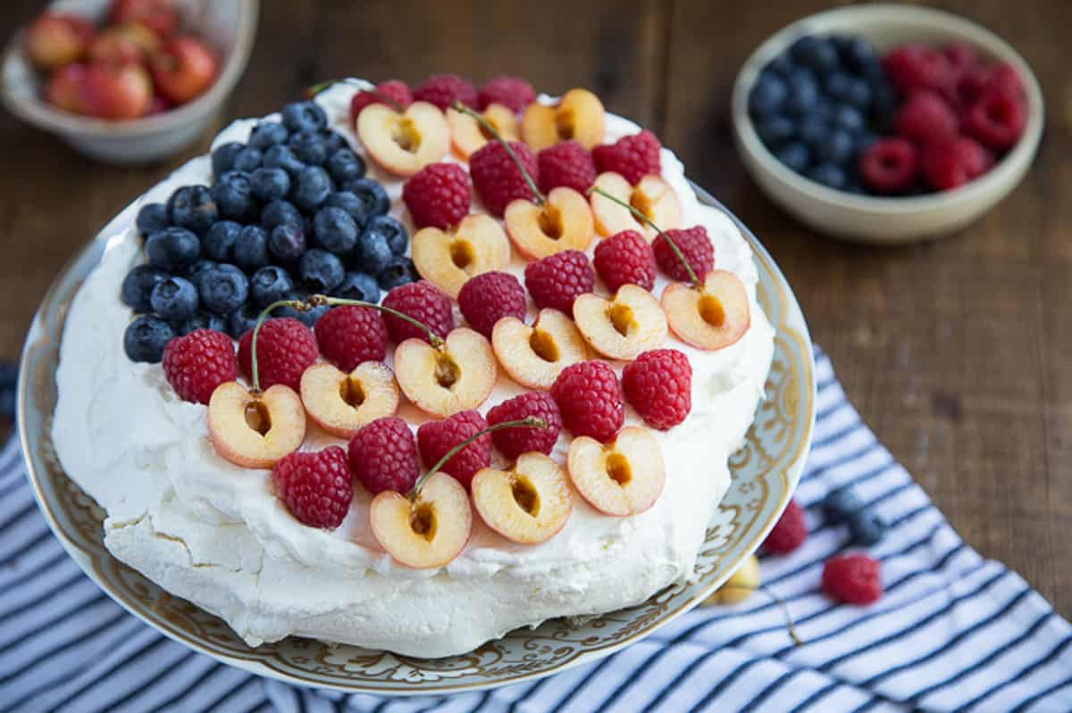 pavlova on a cake stand, decorated with blueberries, cherries, and raspberries in a flag design.