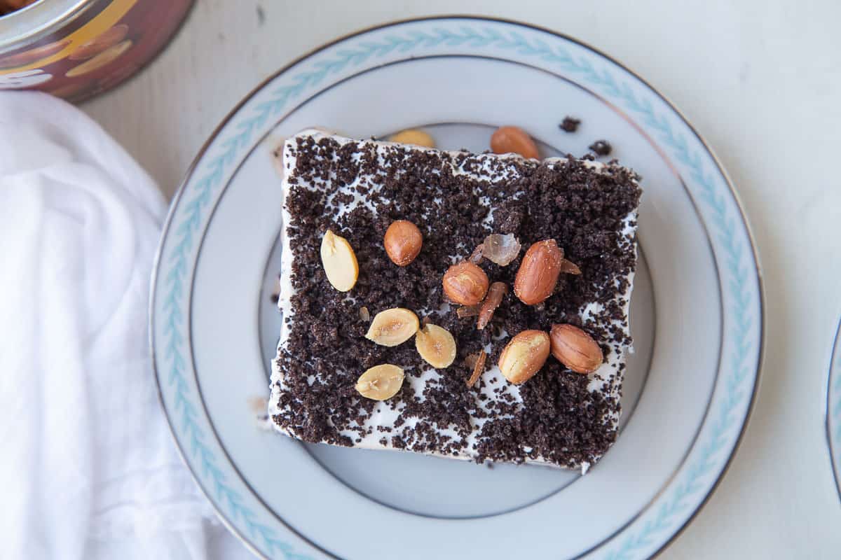 buster bar dessert topped with crushed oreos and peanuts on a white plate with a blue rim.