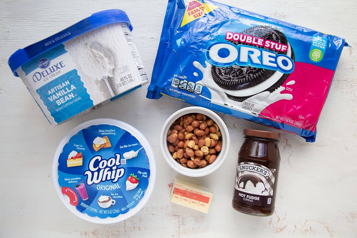 oreos, ice cream, peanuts, whipped topping, and other ingredients on a white table.