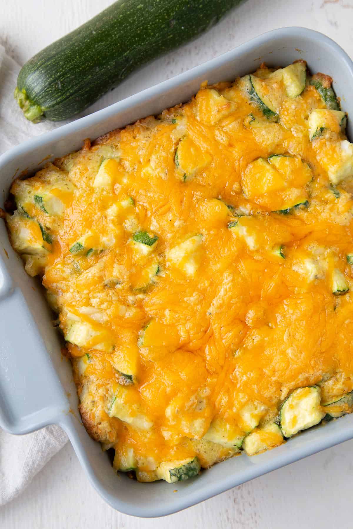 zucchini casserole topped with cheese in a gray square casserole dish.