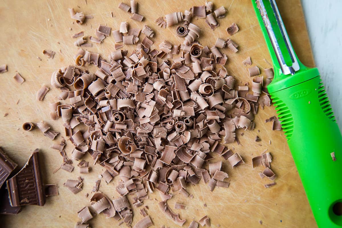 chocolate curls and a green vegetable peeler on a cutting board.