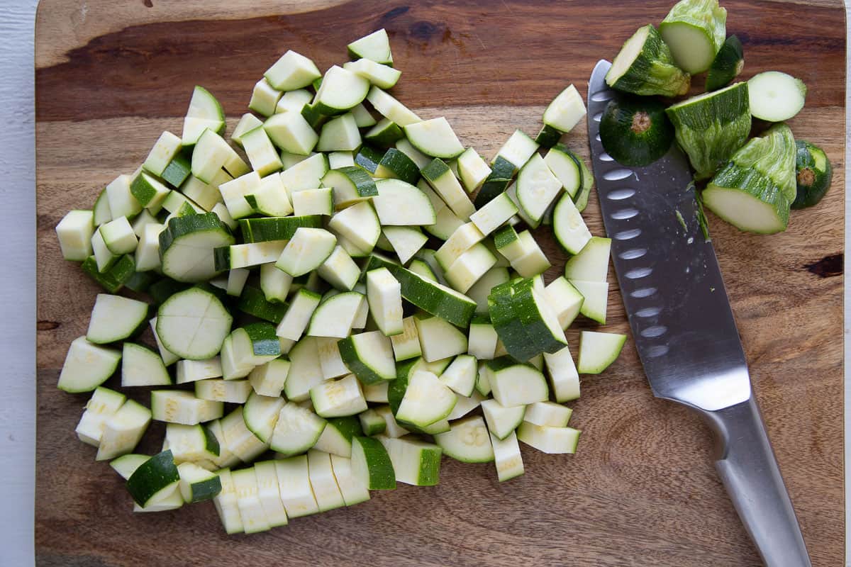 chopped zucchini and a knife on a wooden cutting board.