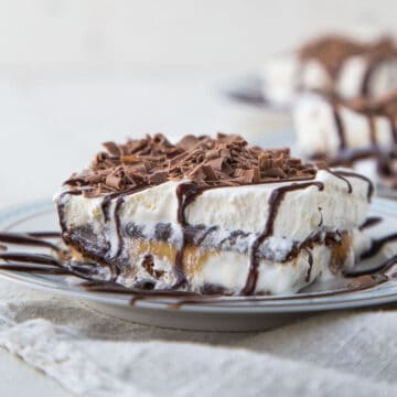 slice of ice cream sandwich dessert topped with chocolate sauce and chocolate curls on a white and blue plate.