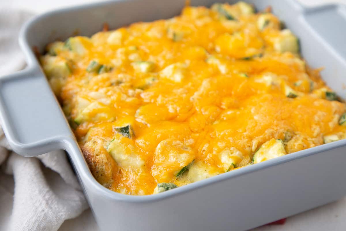 old fashioned zucchini casserole in a gray square casserole dish, topped with cheese.