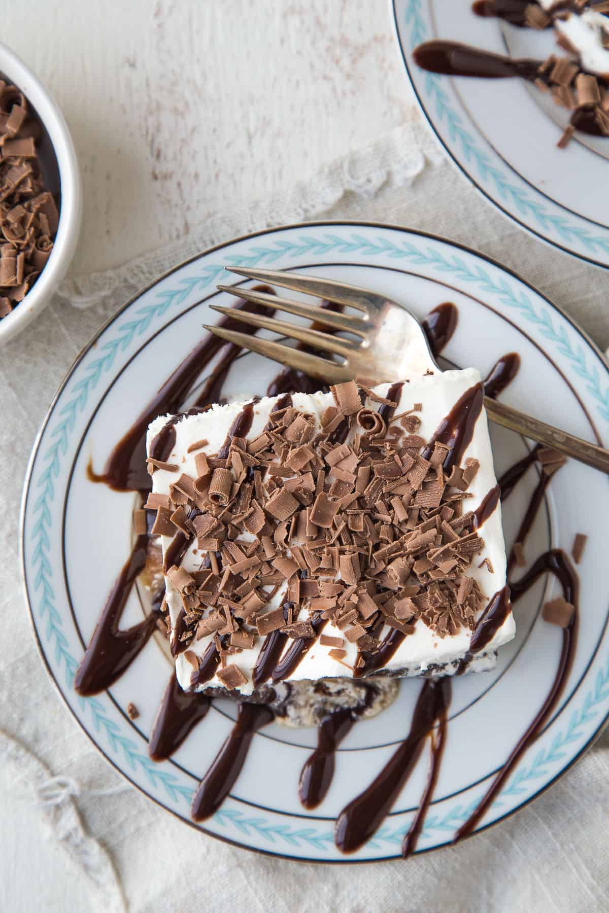 slice of ice cream sandwich dessert on a blue and white plate, topped with chocolate sauce and chocolate curls.