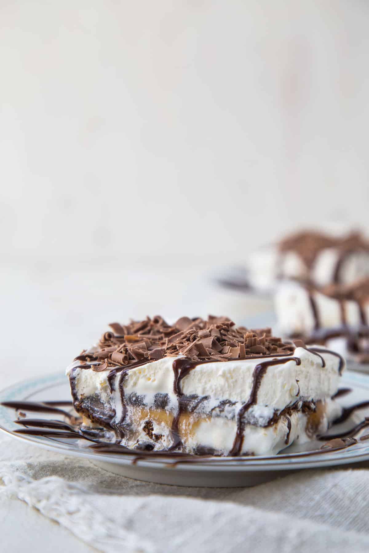 slice of ice cream sandwich dessert on a plate topped with chocolate sauce and chocolate curls.