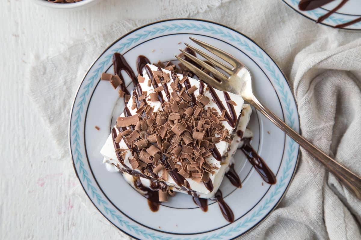 square of an ice cream sandwich dessert on a blue and white plate, topped with drizzles of chocolate sauce and small chocolate curls.