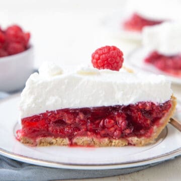 slice of no-bake raspberry pie topped with whipped cream and a single raspberry on a white plate.