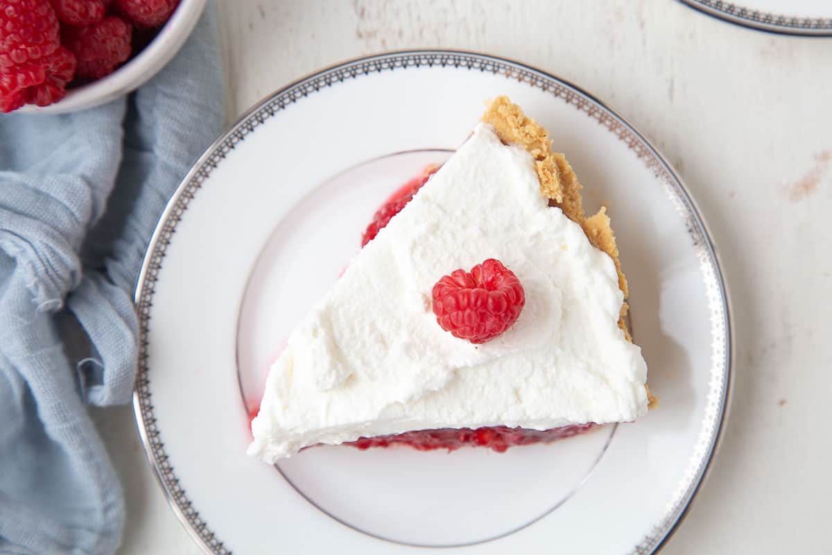 slice of raspberry pie with whipped cream and a fresh raspberry on top.