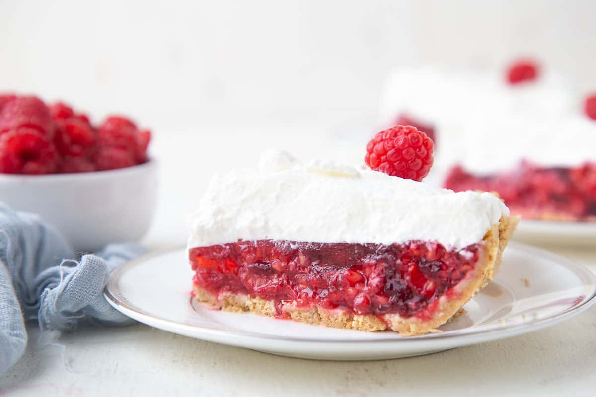 slice of no-bake raspberry pie with whipped cream and fresh raspberry on top.