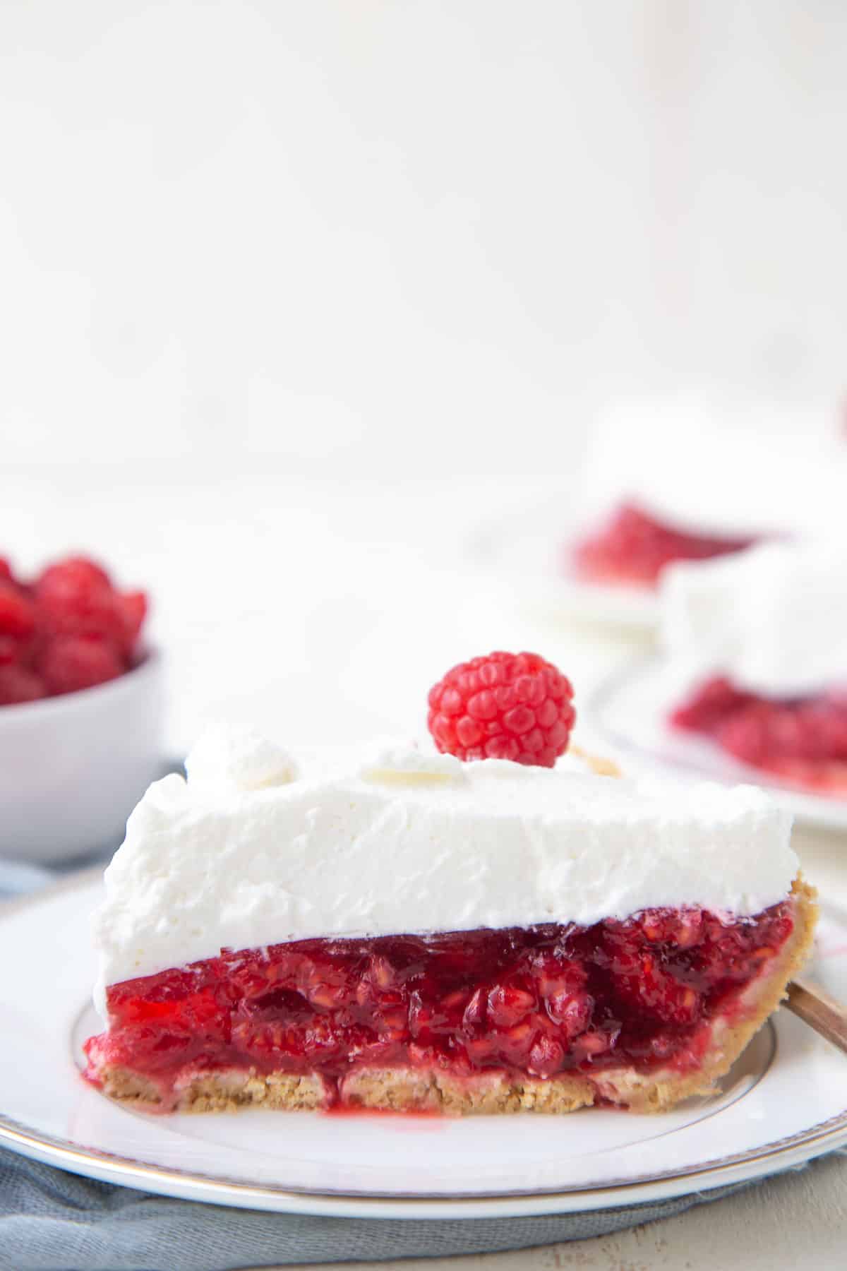 slice of no-bake raspberry pie topped with whipped cream on a white plate.