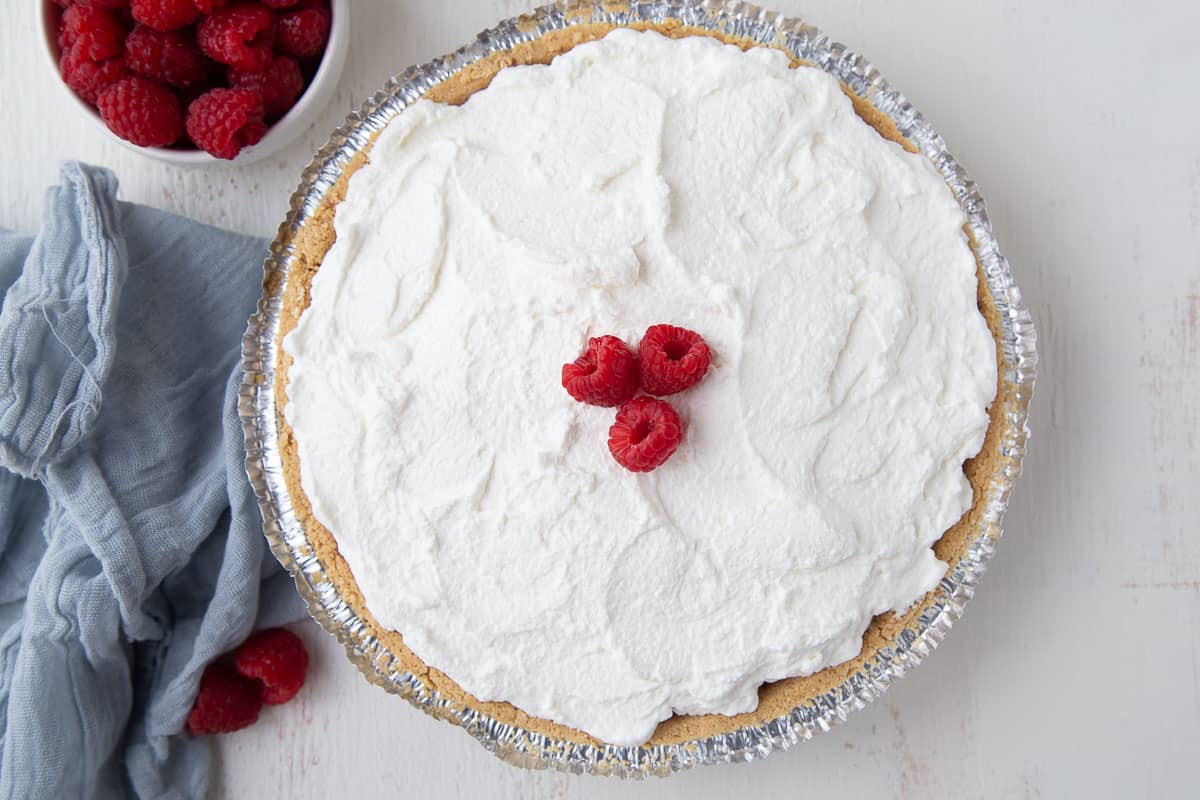 whole raspberry pie topped with whipped cream and three fresh raspberries.