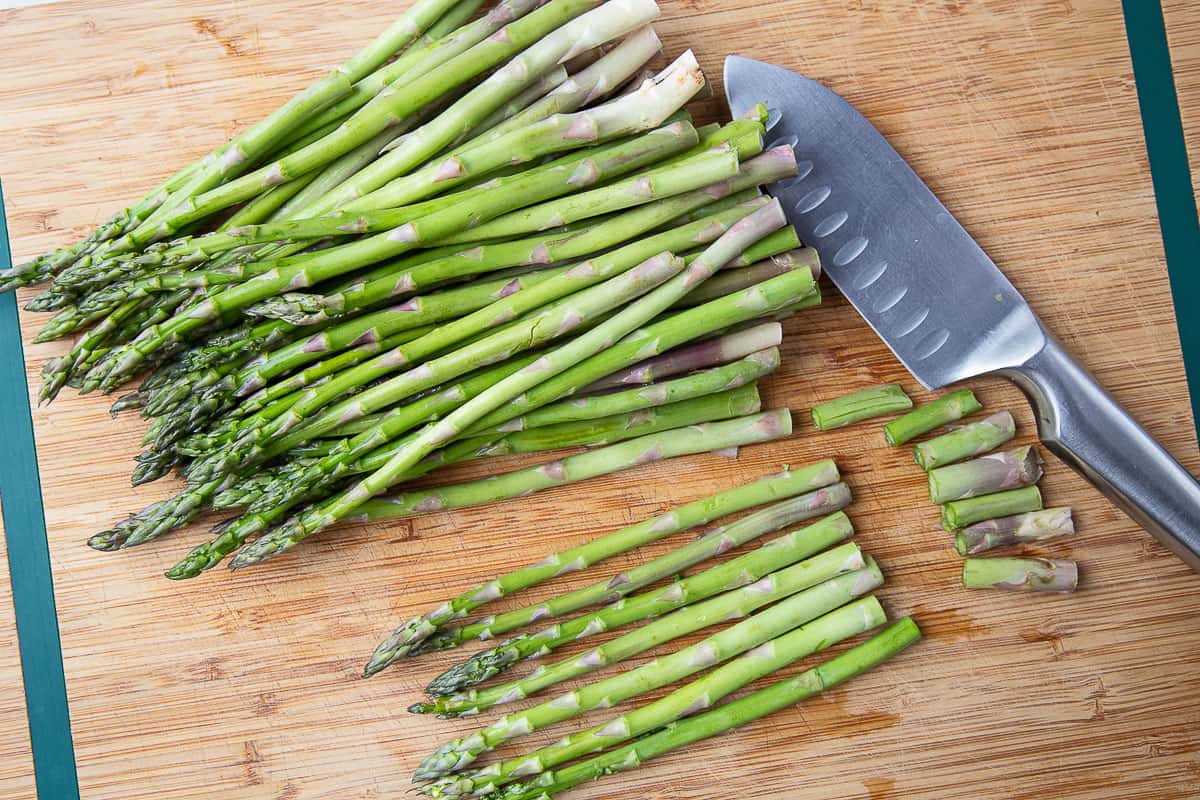 a knife and asparagus on a wooden cutting board.