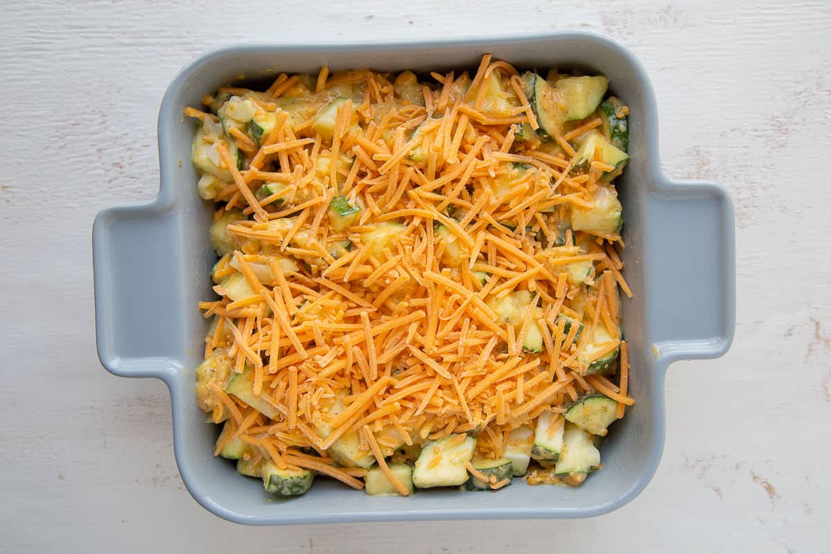 casserole dish filled with raw zucchini and topped with shredded cheddar.