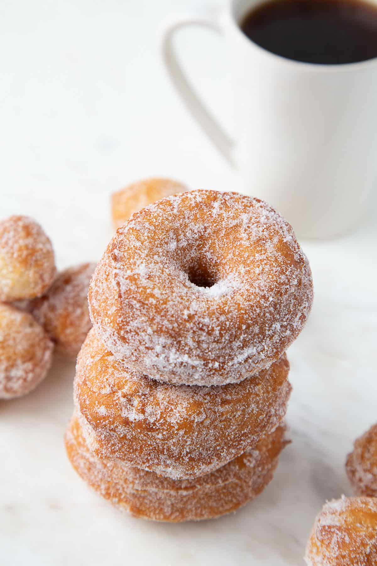 3 biscuit donuts stacked next to donut holes and a mug of black coffee.