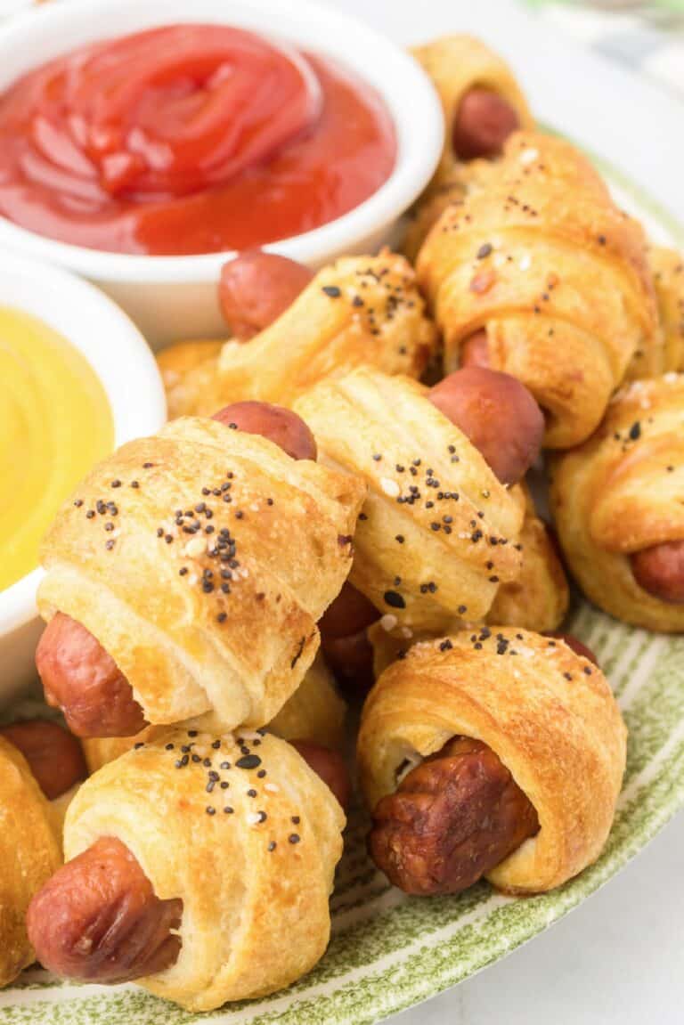 pigs in a blanket on a platter with little bowls of ketchup and mustard.