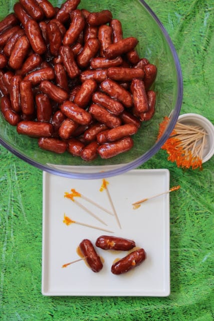 mini cocktail sausages in a large bowl, next to three sausages with toothpicks on a white plate.