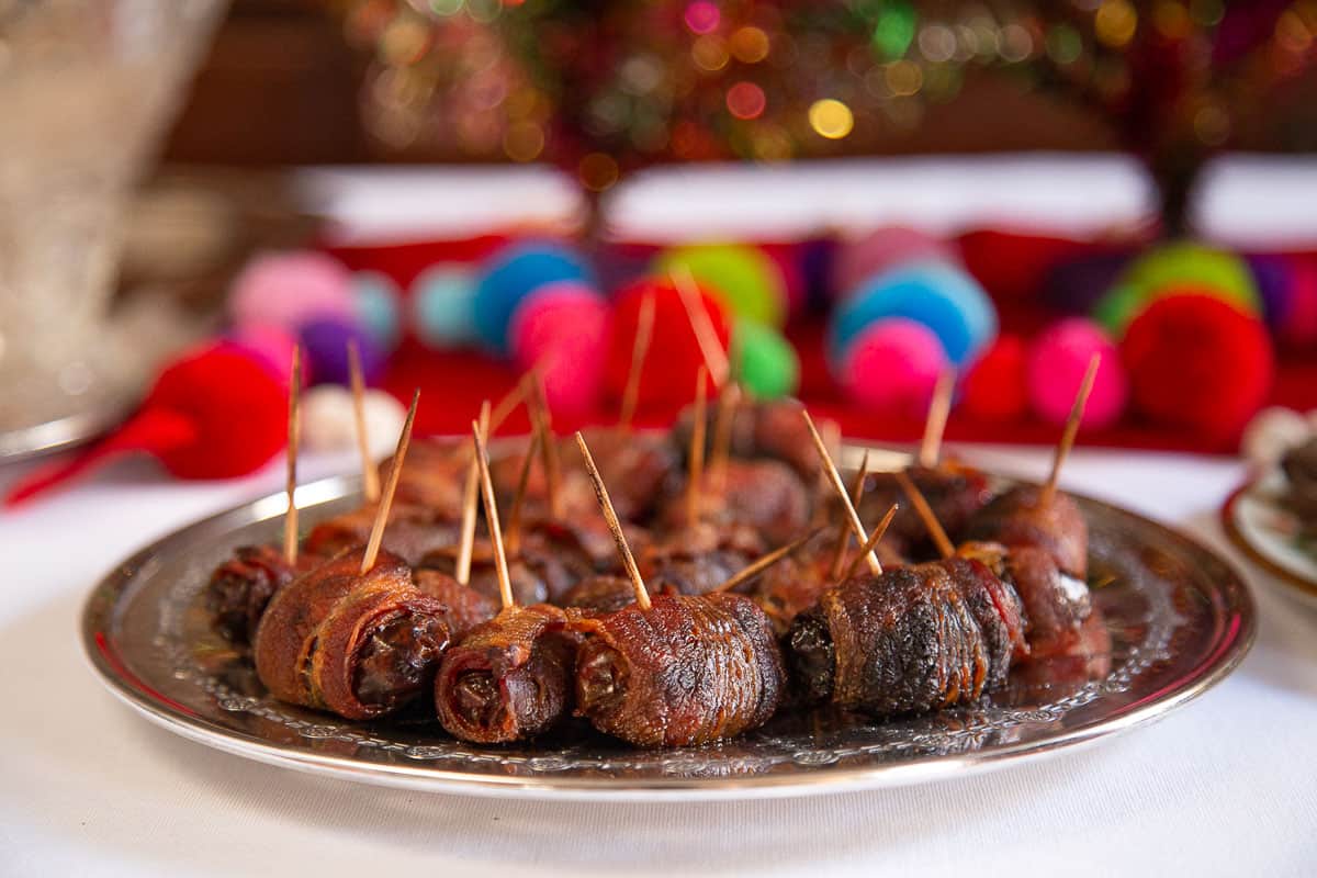 bacon wrapped dates secured with toothpicks on a metal plate.