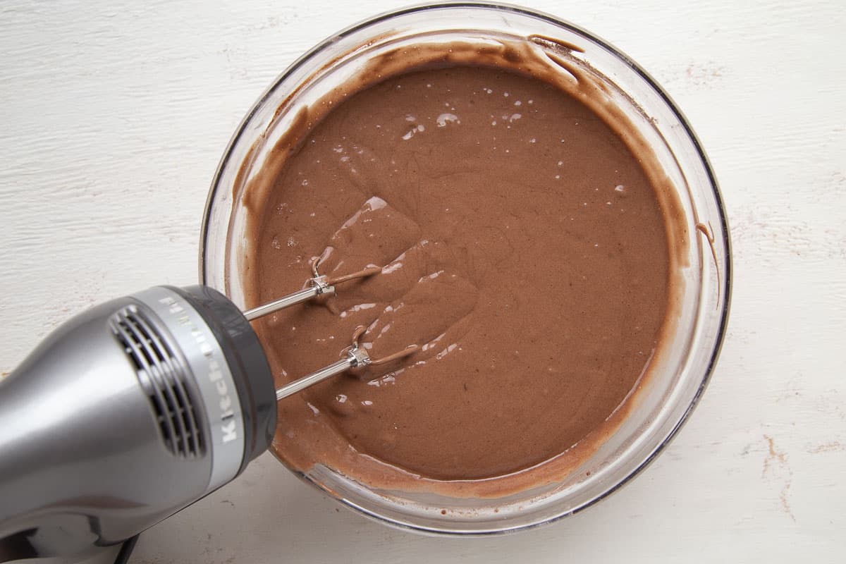 chocolate cake batter in a glass bowl with a hand mixer.