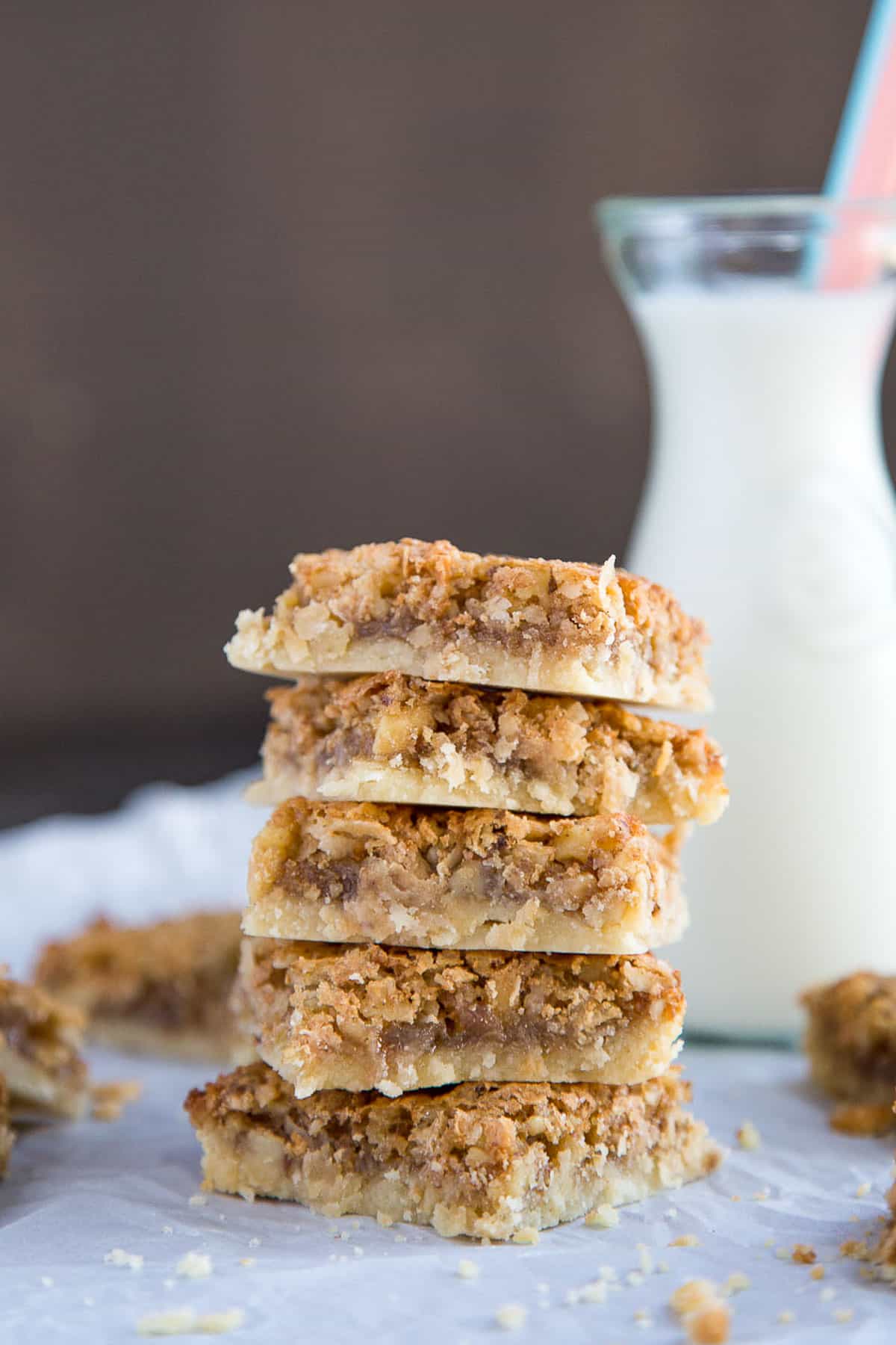 five chewy coconut bar cookies stacked up next to a glass of milk with a pink straw.