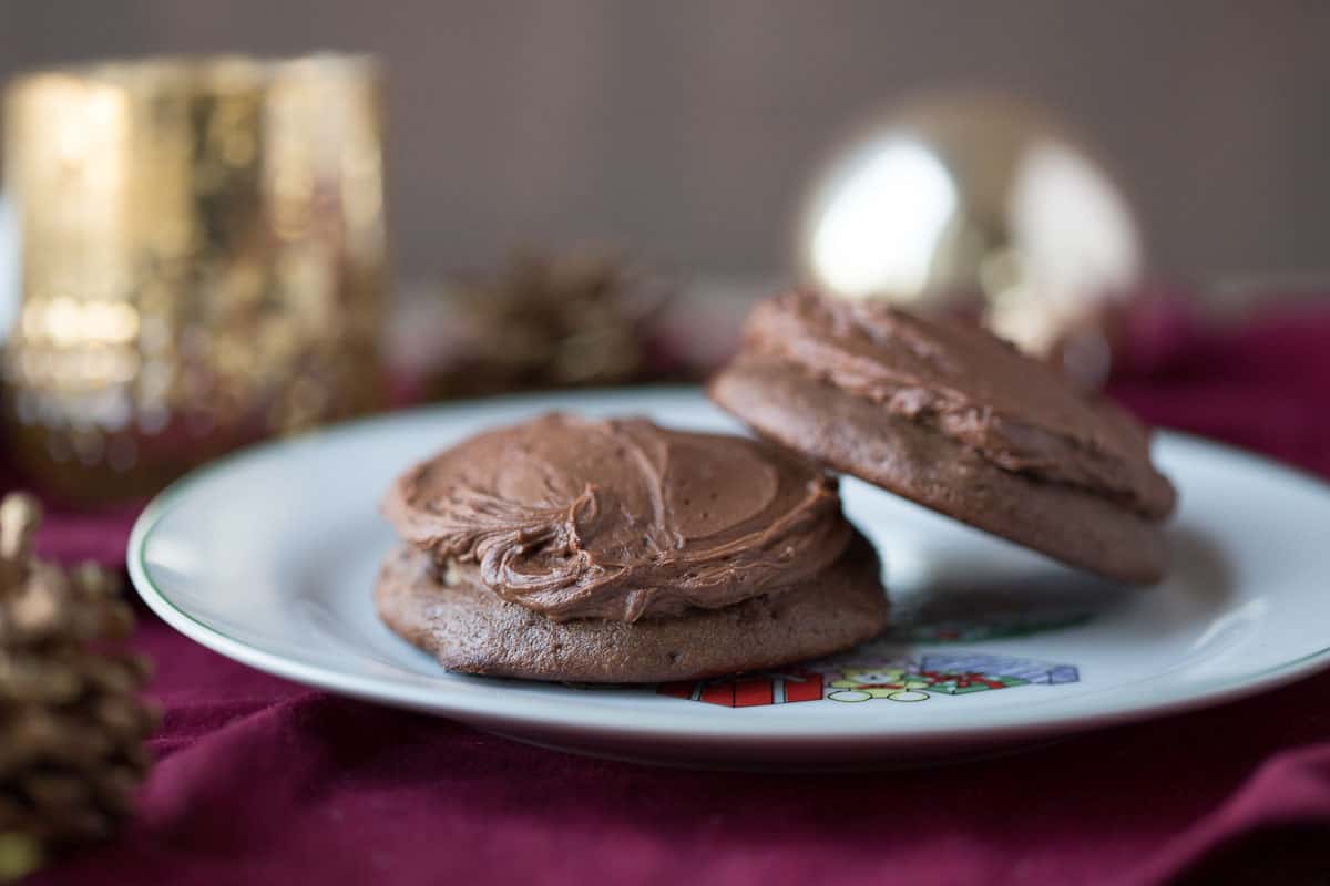 two chocolate drop cookies with frosting on a white plate.