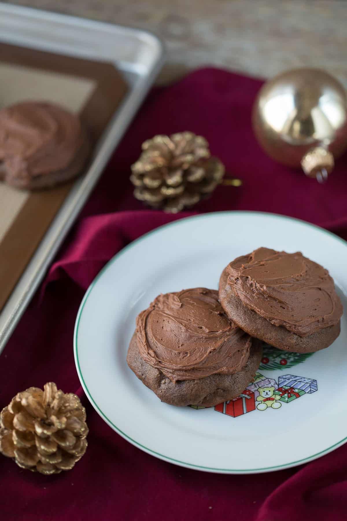 cocoa drop cookies on a white plate on a burgundy tablecloth next to pinecones and a gold christmas ball.