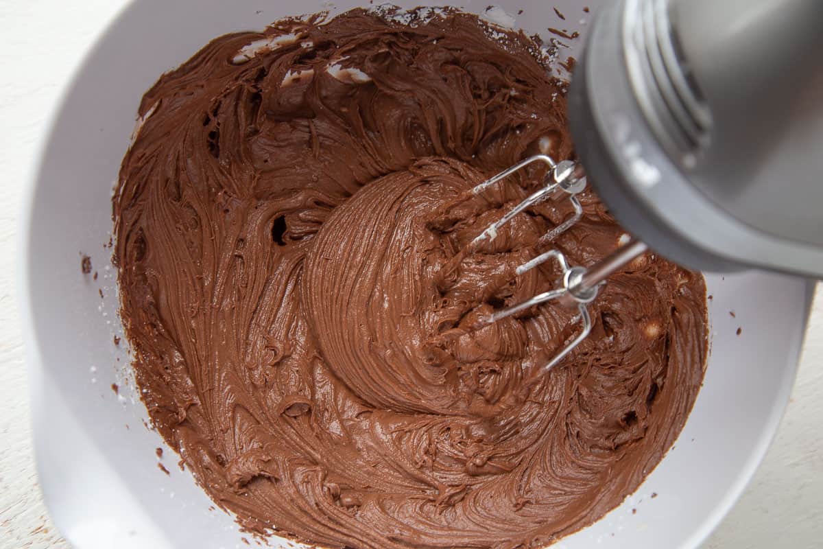 homemade chocolate frosting in a white bowl with a hand mixer.