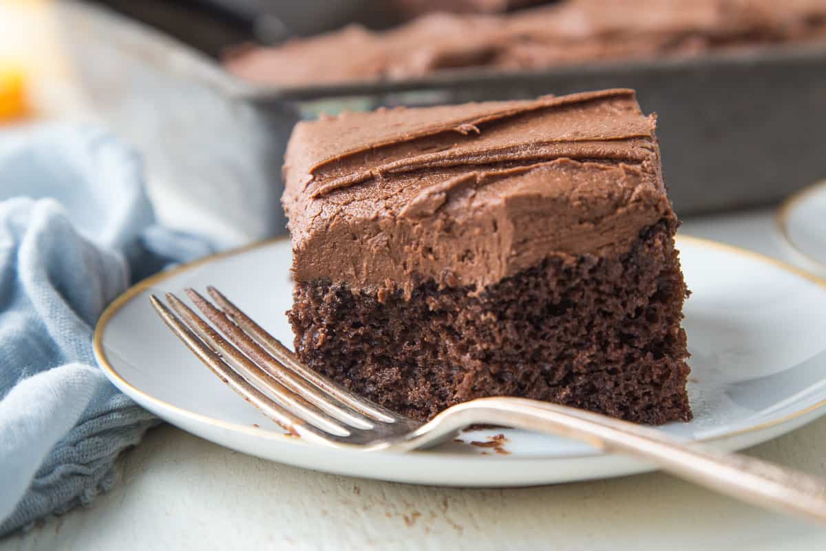 slice of chocolate mayo cake on a white plate next to a fork, with a bite taken out.