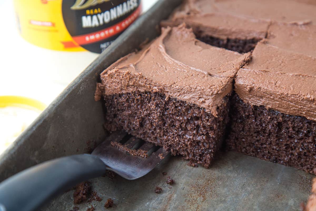 a spatula lifting a slice of chocolate mayonnaise cake out of a metal pan.