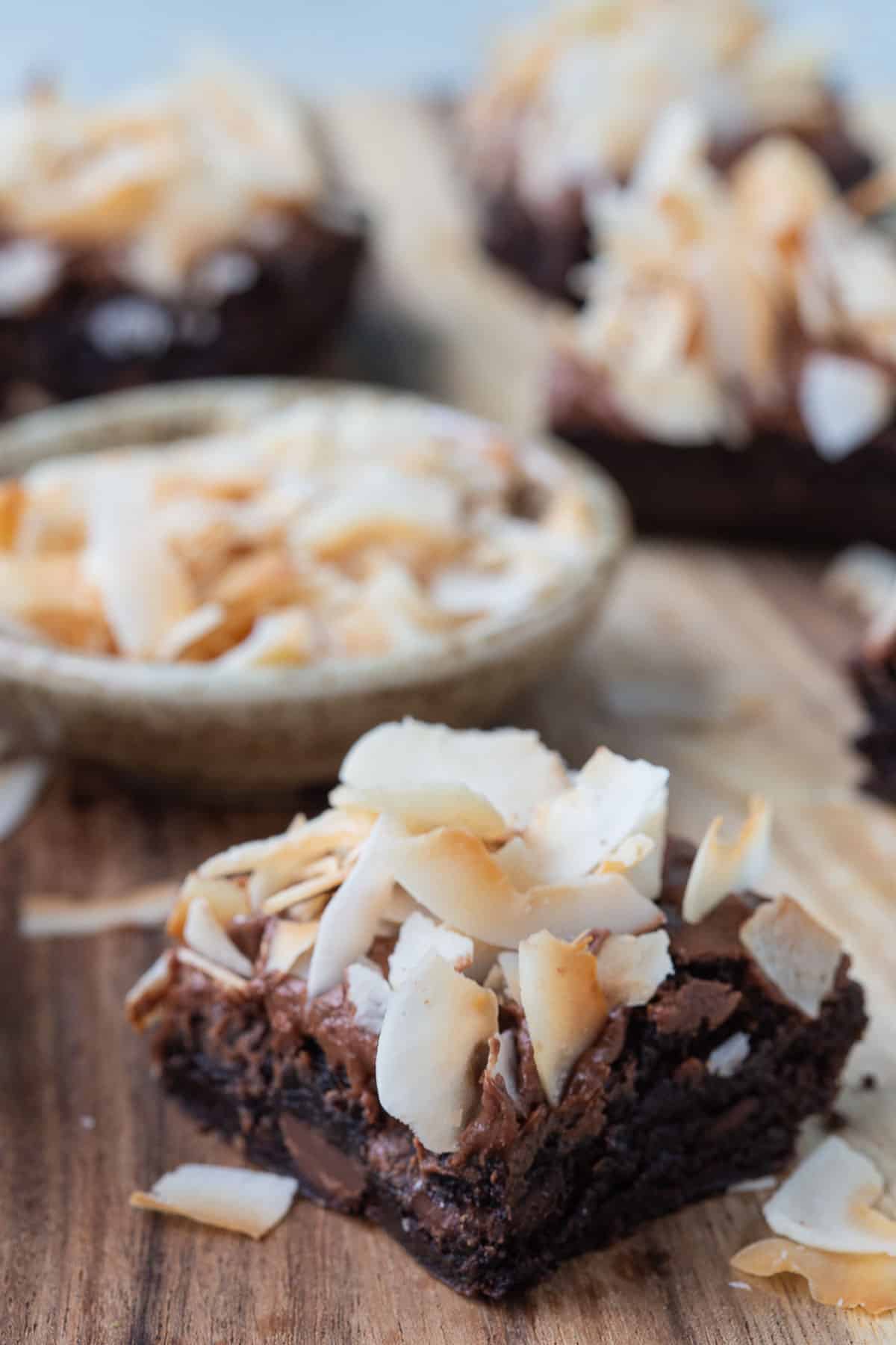 brownies topped with frosting and coconut shavings on a wooden board.