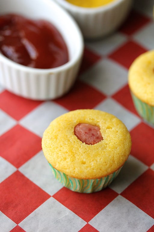 corn muffins with a cocktail sausage in the middle, next to a bowl of bbq sauce.