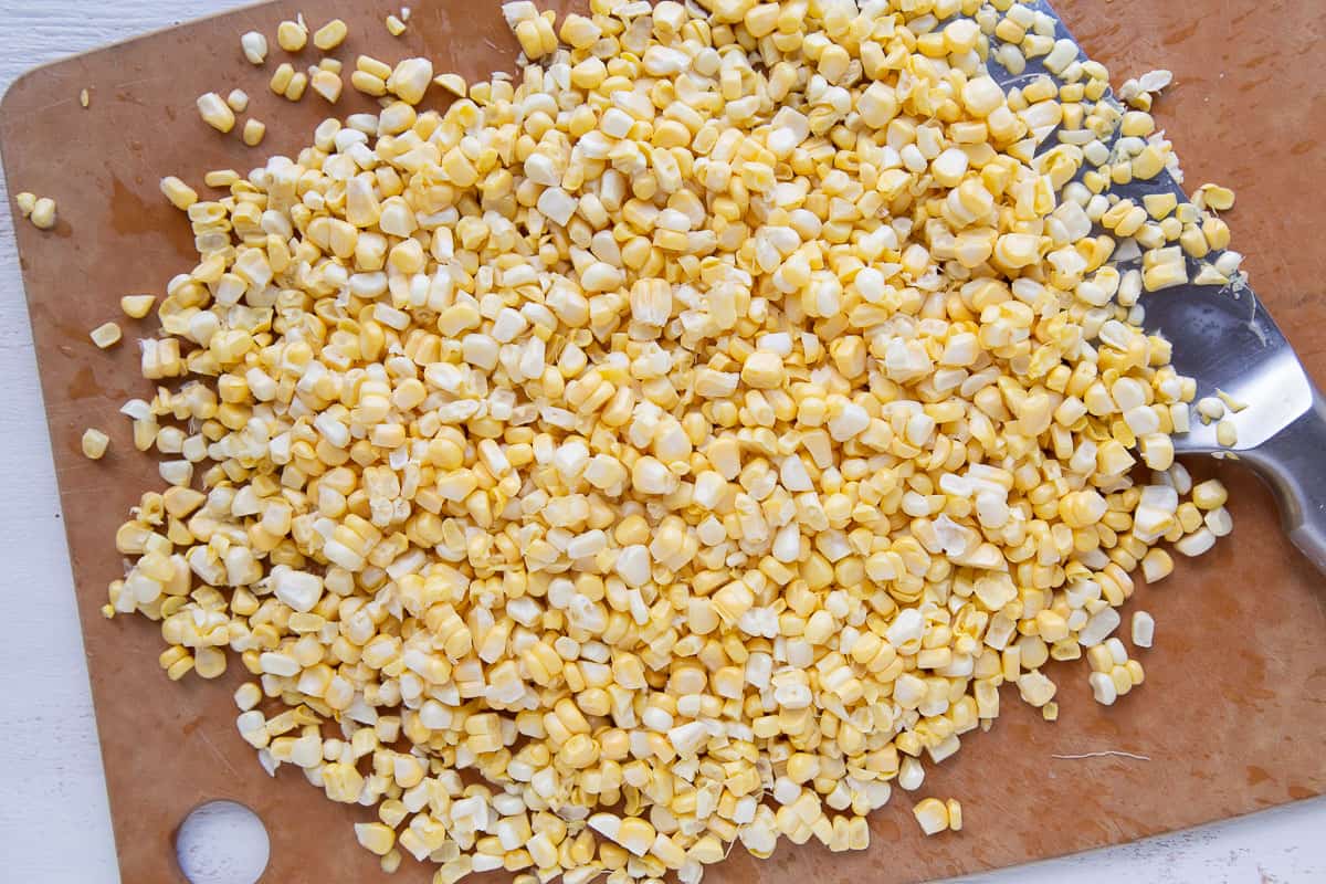 chopped corn kernels on a wooden cutting board with a knife.