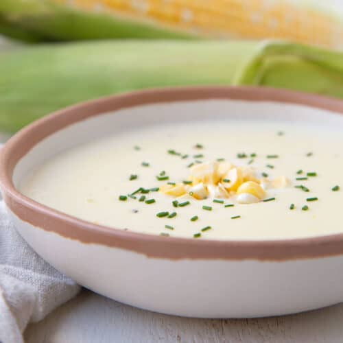 cream of corn soup in a low bowl, topped with corn kernels and chives.