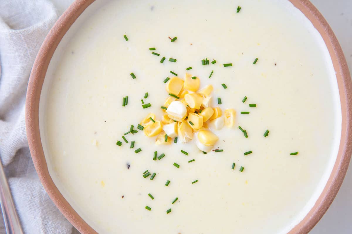 bowl of cream of corn soup topped with chives and corn kernels.