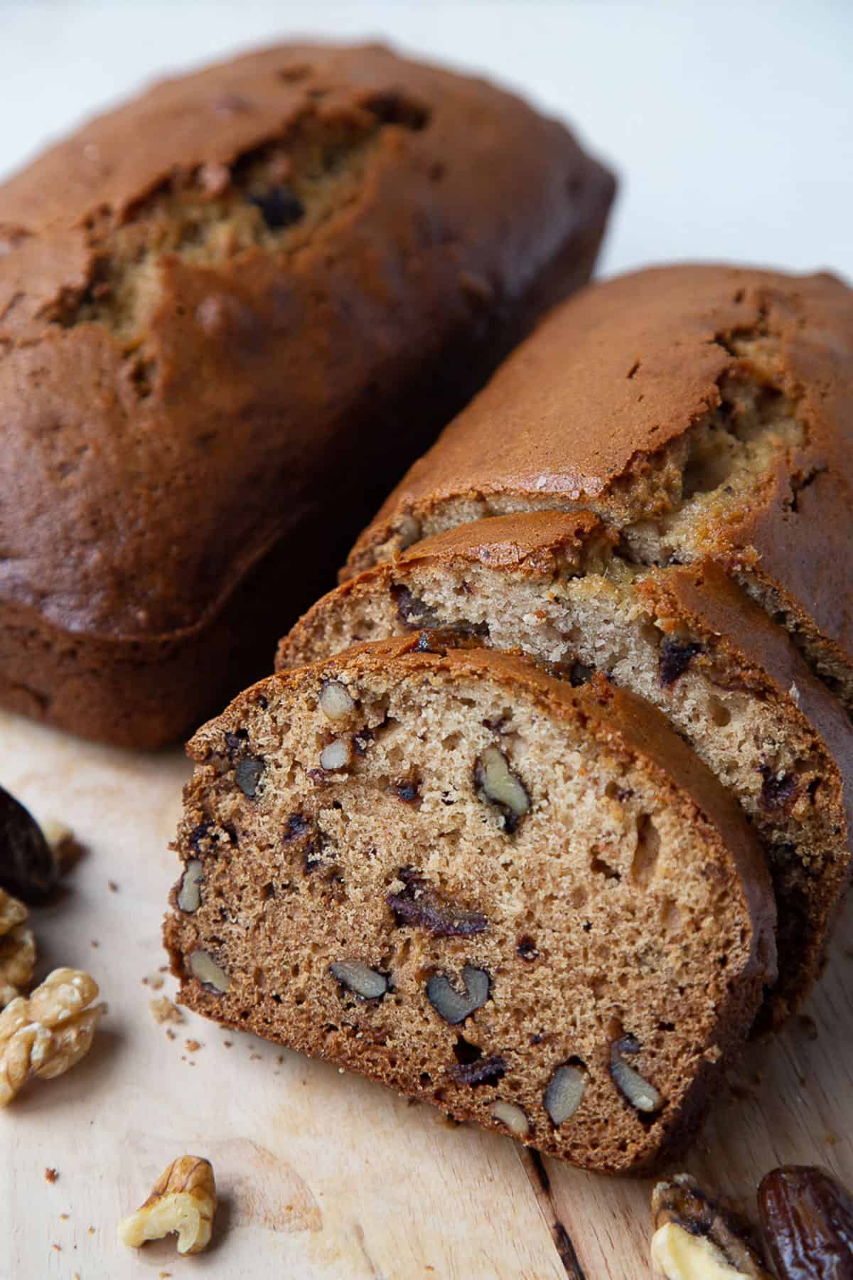 two loaves of date nut bread on a wooden board, one with slices cut out.