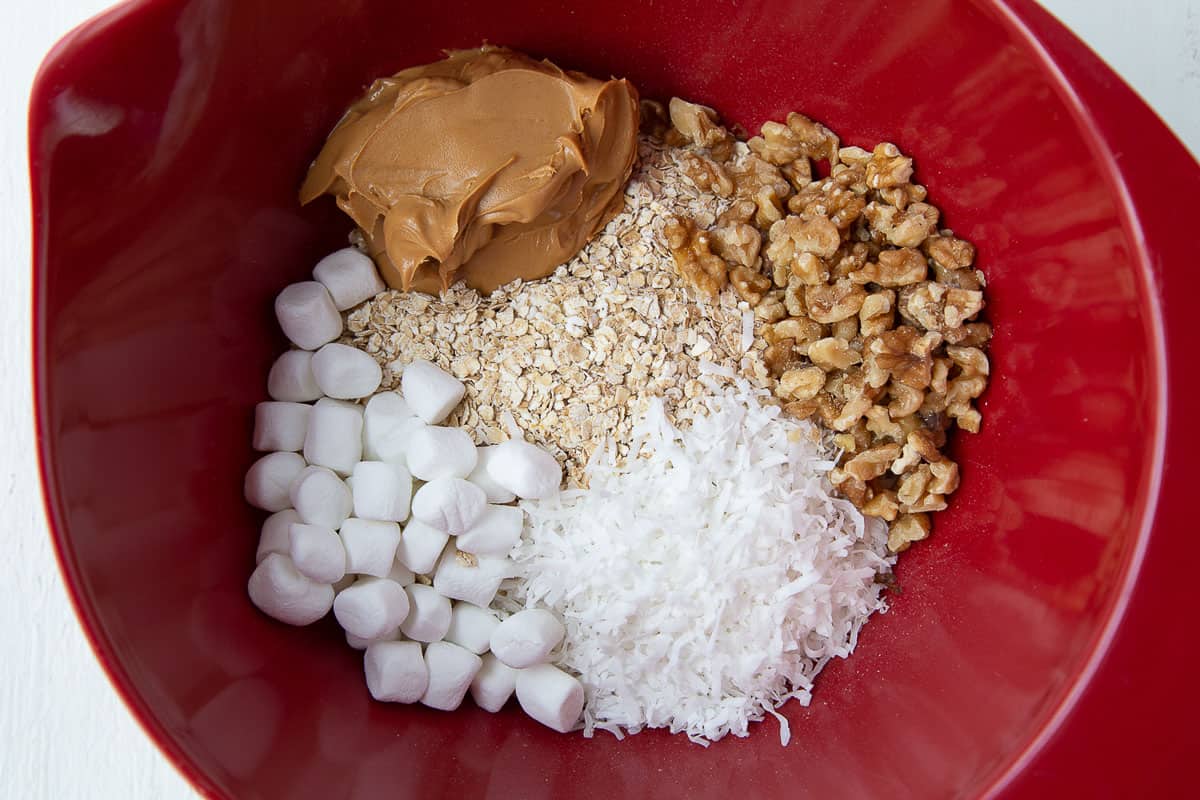 oats, peanut butter, coconut, walnuts, and marshmallows in a big red bowl.