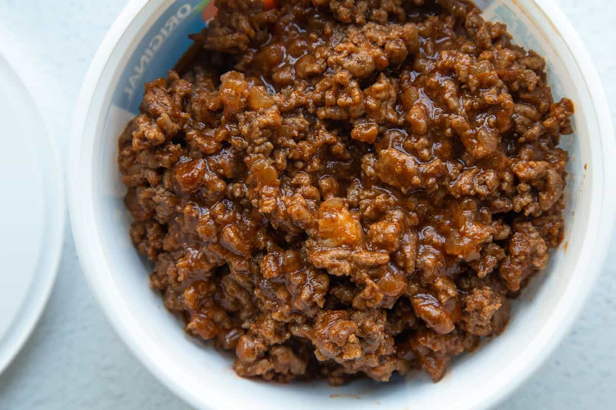 sloppy joe meat in a white plastic container next to a lid.