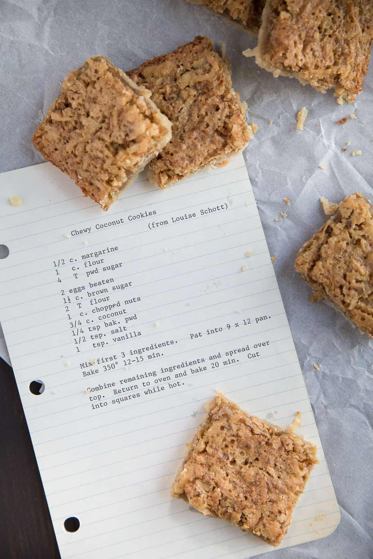 lined notebook paper with a typewriter written recipe for coconut bars, surrounded by squares of coconut bar cookies. 