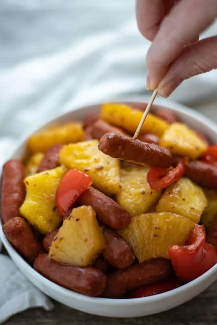 little smokies, pineapple chunks, and red pepper pieces in a white bowl.