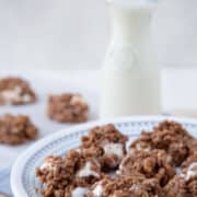 no bake boiled cookies on a white plate next to a glass of milk with a straw.