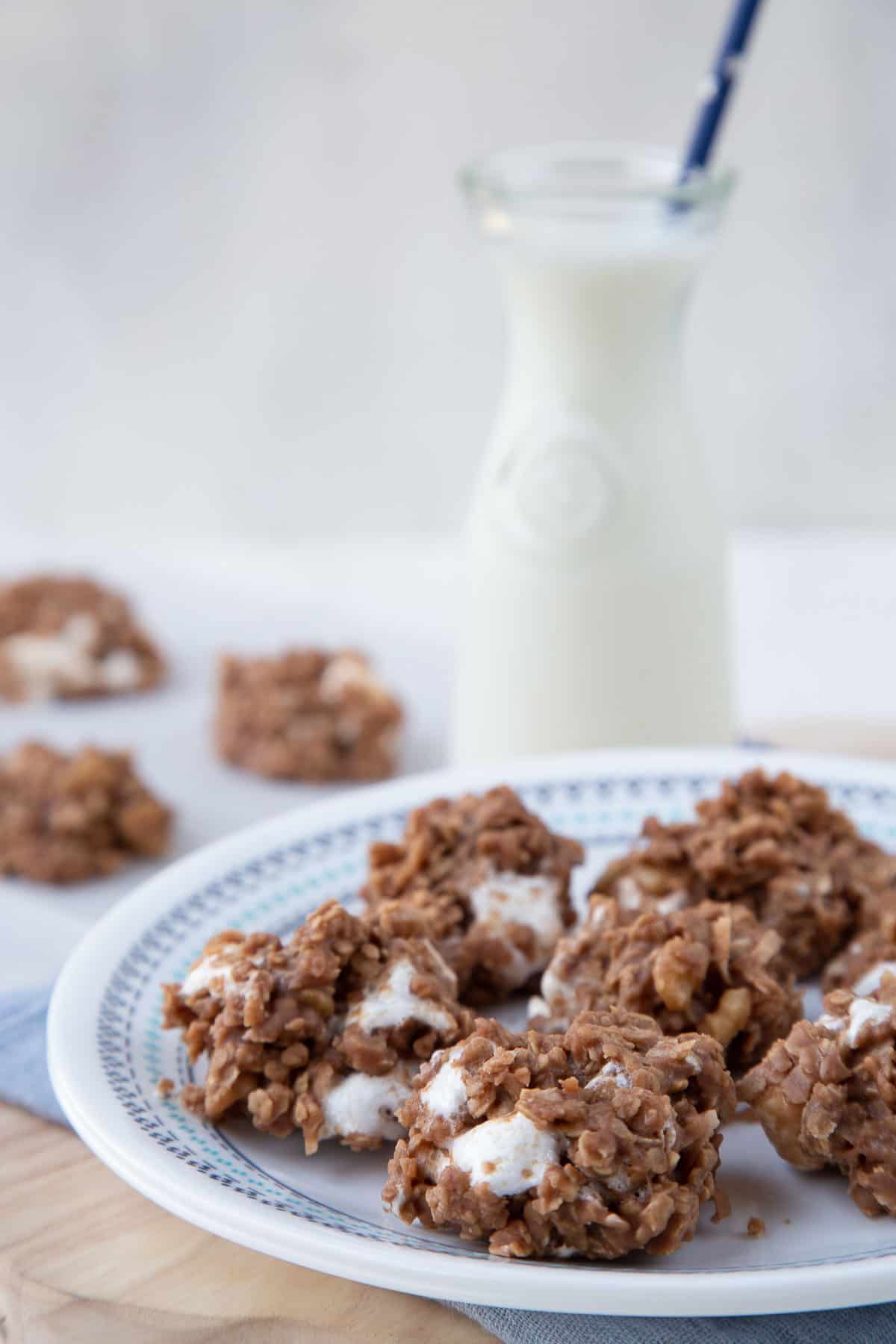 no bake boiled cookies on a white plate next to a glass of milk with a straw.
