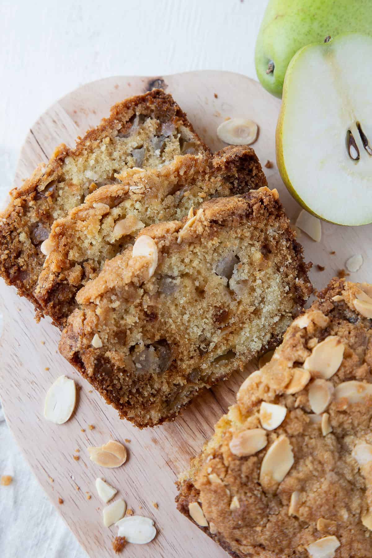 three slices of pear bread next to a whole loaf on a decorative wooden board.