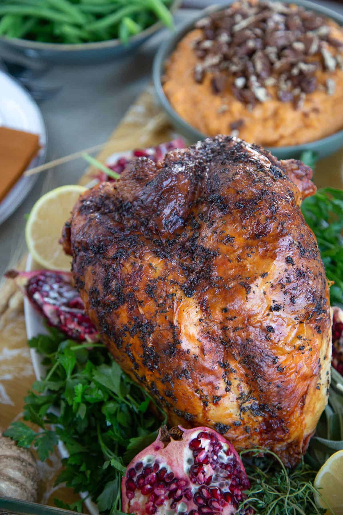 bone-in turkey breast with golden crispy skin, on a bed of herbs with a pomegranate cut open on the platter.