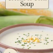 creamy soup in a bowl with corn kernels and chives on top.