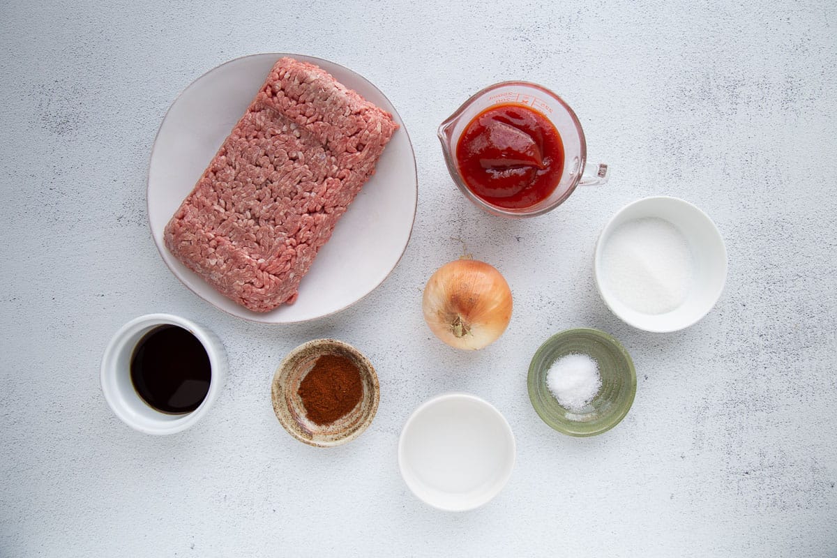 ground beef, ketchup, and small bowls of other ingredients on a white table.