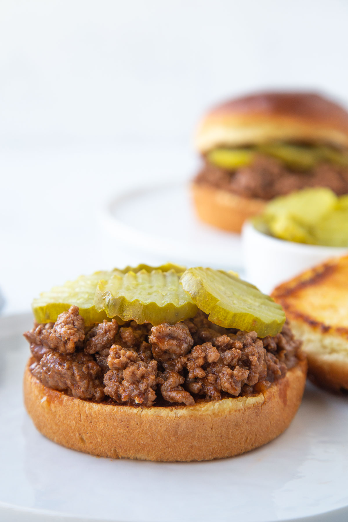 open faced sloppy joe topped with pickles on a bun.